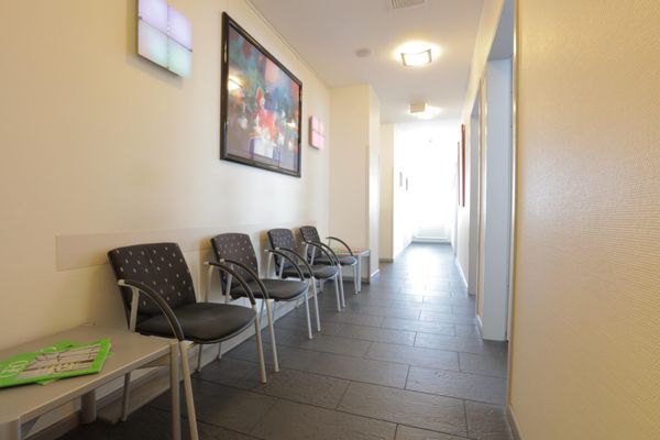 Ein heller Wartebereich mit mehreren Stühlen, die entlang der Wand in einem Flur aufgereiht sind. An der Wand hängt ein farbenfrohes, modernes Kunstwerk.